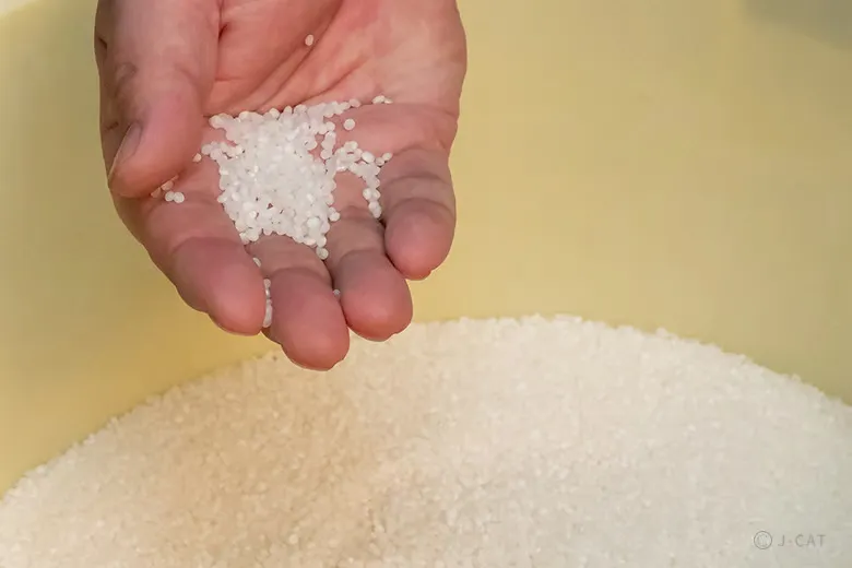 Close-up of a brewer's open hand cradling a small pile of highly polished white sake rice grains above a storage container, highlighting the meticulous milling fractions discussed on a private tour at Sasaki Shuzo in Kyoto.