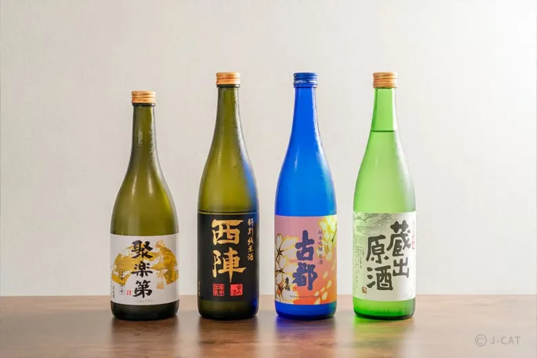 A minimalist lineup of four elegant premium sake bottles from Sasaki Shuzo including Jurakudai Junmai Daiginjo, Nishijin, and Koto labels neatly displayed on a warm wooden table for a private tasting class.