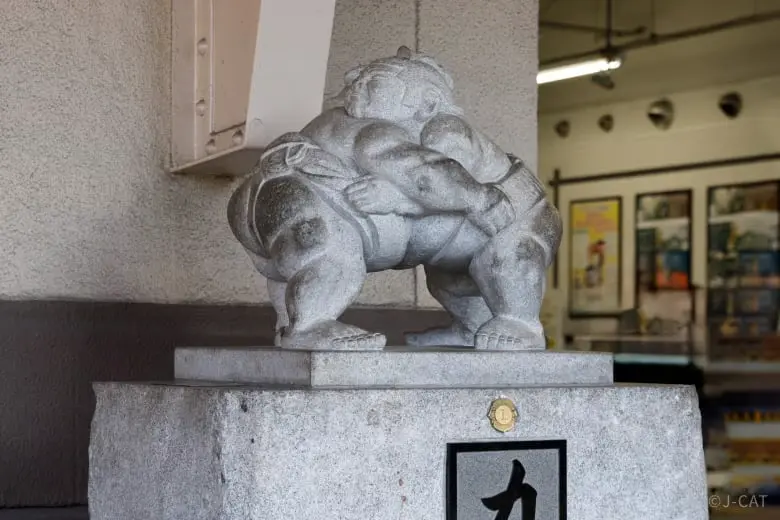 experiences_tokyo_ryogoku-sumo-stone-statue A carved stone statue of a professional sumo wrestler crouched in a low, powerful stance outside near Ryogoku Station, representing the rich sumo heritage of the historic Ryogoku neighborhood in Tokyo.
