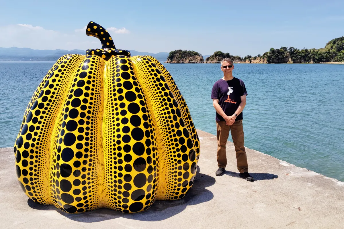Rob Dyer, founder of The Real Japan, standing on a concrete pier on the right of Yayoi Kusama’s famous yellow and black dotted outdoor pumpkin sculpture on the art island of Naoshima, Seto Inland Sea.