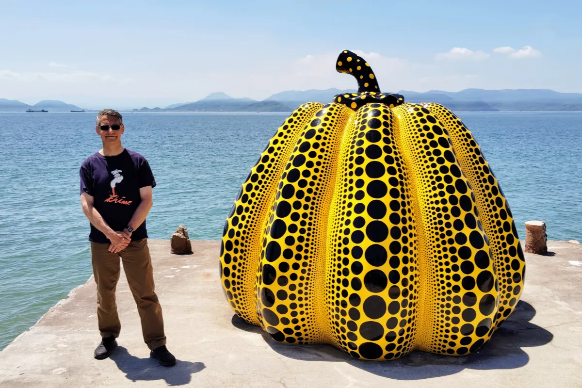 Rob Dyer, founder of The Real Japan, standing on a concrete pier on the left of Yayoi Kusama’s famous yellow and black dotted outdoor pumpkin sculpture on the art island of Naoshima, Seto Inland Sea.