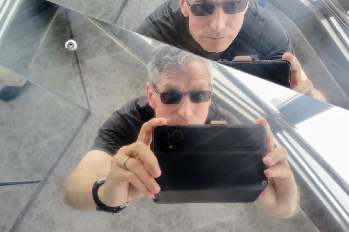 An artistic, multi-angled reflection selfie taken by Rob Dyer using his smartphone against mirrored glass panels, wearing sunglasses and a black t-shirt during a city observation tour at Tokyo Tower.