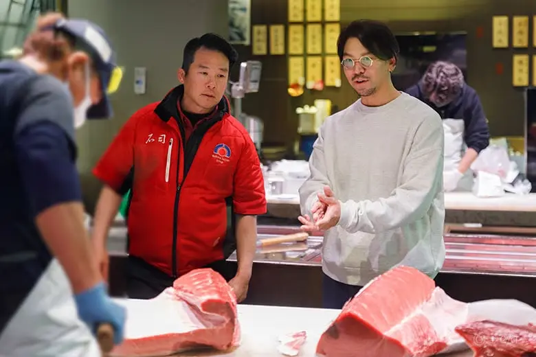 toyosu-fish-market-tour-guide-talks-with-expert-fishmonger A specialist interpreter and industry guide stands on the active wholesale inner floor talking with an elite merchant in a red jacket, analyzing the day’s fresh bluefin tuna catches before morning transactions begin during a private wholesale floor tour at Toyosu Market in Tokyo